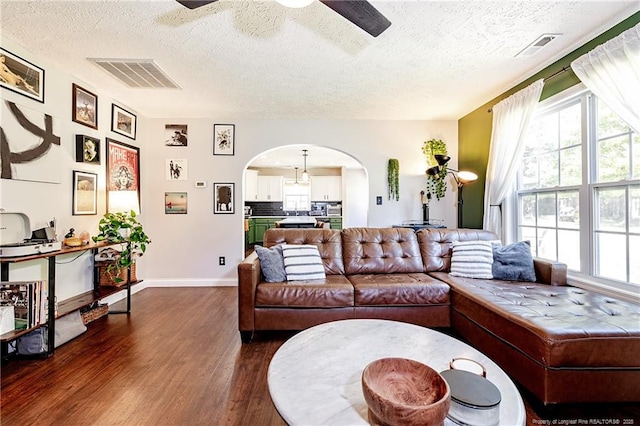 living area featuring a healthy amount of sunlight, a ceiling fan, a textured ceiling, arched walkways, and dark wood-type flooring