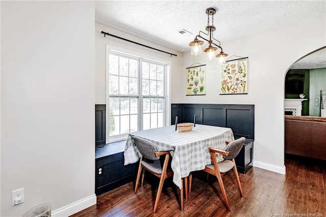 dining area with arched walkways, dark wood finished floors, a textured ceiling, and visible vents