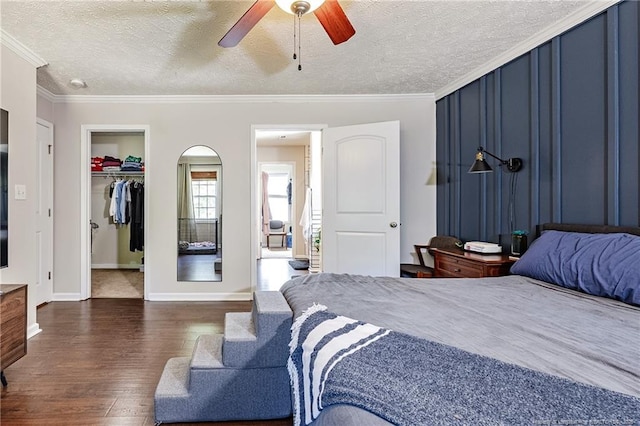bedroom featuring crown molding, a walk in closet, a textured ceiling, a ceiling fan, and dark wood-style floors