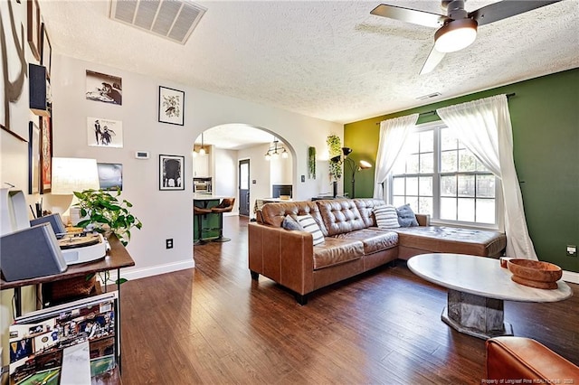 living room featuring arched walkways, a textured ceiling, visible vents, and dark wood finished floors