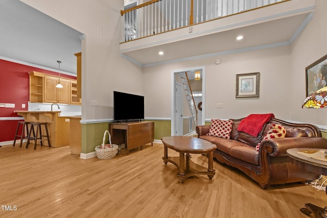 living area with baseboards, ornamental molding, light wood-style flooring, and a high ceiling