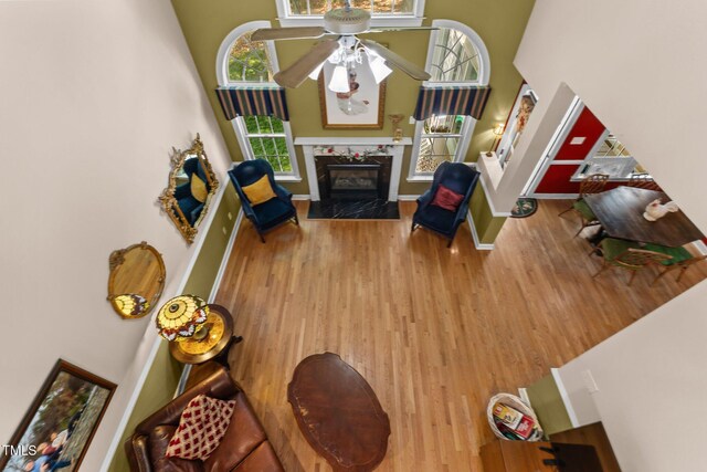 living room with wood finished floors, a fireplace, baseboards, a high ceiling, and a ceiling fan