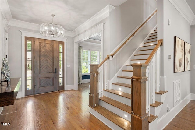 entryway with hardwood / wood-style flooring, stairway, a chandelier, baseboards, and crown molding