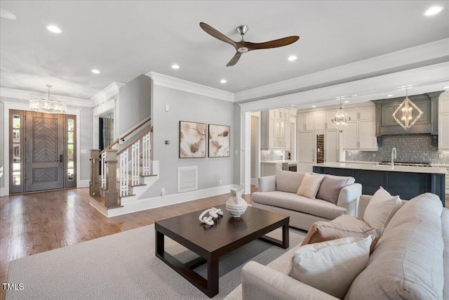 living area featuring a chandelier, baseboards, ornamental molding, a ceiling fan, and stairs
