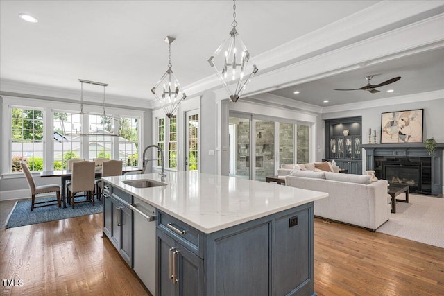 kitchen featuring a sink, stainless steel dishwasher, a chandelier, ornamental molding, and a glass covered fireplace