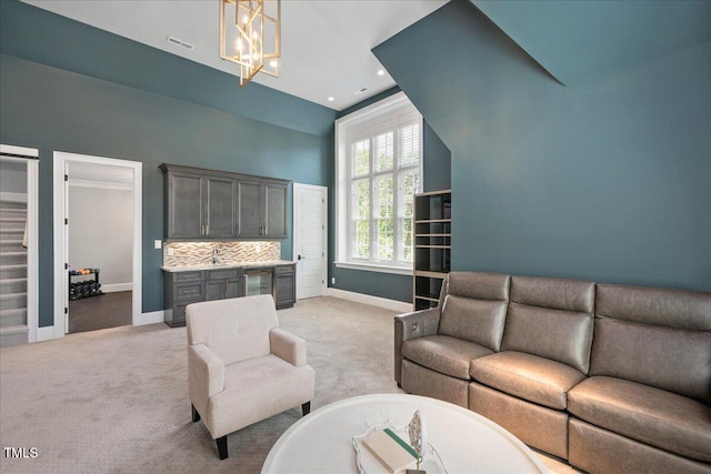 living area with baseboards, light carpet, a chandelier, stairs, and high vaulted ceiling