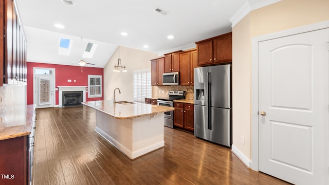 kitchen featuring a sink, stainless steel appliances, tasteful backsplash, vaulted ceiling with skylight, and a fireplace