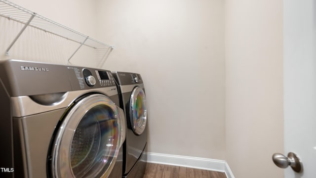 clothes washing area with baseboards, laundry area, washer and dryer, and wood finished floors