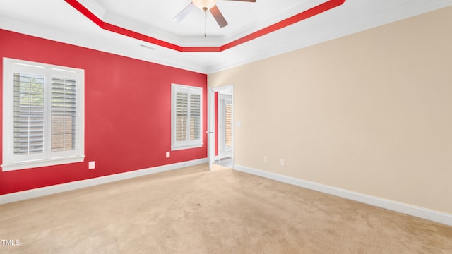 carpeted spare room featuring a tray ceiling, crown molding, baseboards, and a ceiling fan