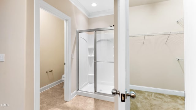 bathroom with toilet, baseboards, a shower stall, crown molding, and a walk in closet