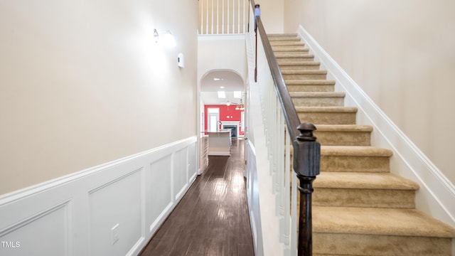 stairway featuring arched walkways, a towering ceiling, a wainscoted wall, and wood finished floors