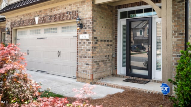 view of exterior entry with metal roof, a garage, a standing seam roof, and brick siding