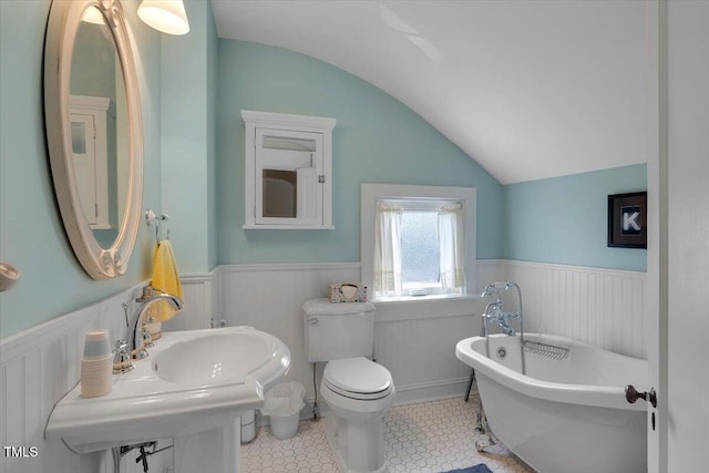 bathroom with a freestanding tub, wainscoting, a sink, toilet, and lofted ceiling
