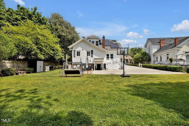 rear view of house with fence, stairs, roof mounted solar panels, a patio area, and a yard