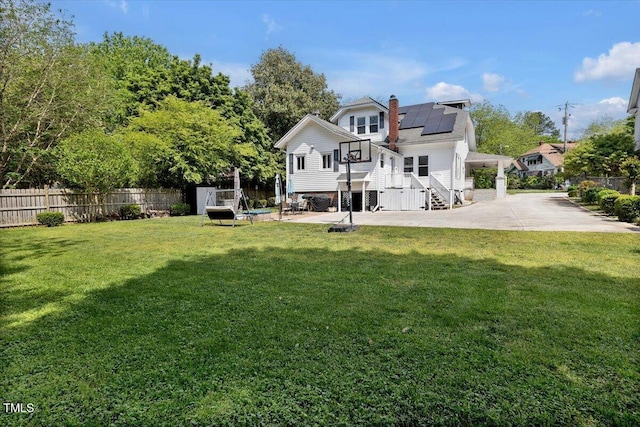 rear view of house featuring a patio, a lawn, fence, and solar panels