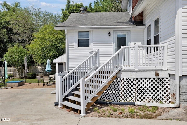 property entrance with fence, outdoor dining space, a patio area, and roof with shingles