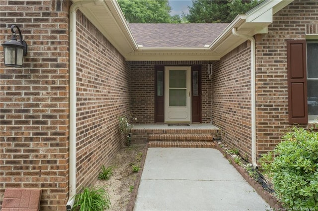 doorway to property featuring brick siding and a shingled roof