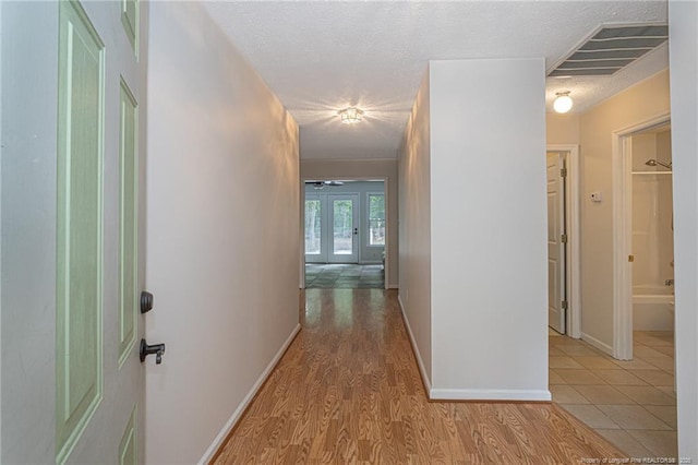 hall featuring french doors, a textured ceiling, visible vents, baseboards, and light wood-style flooring