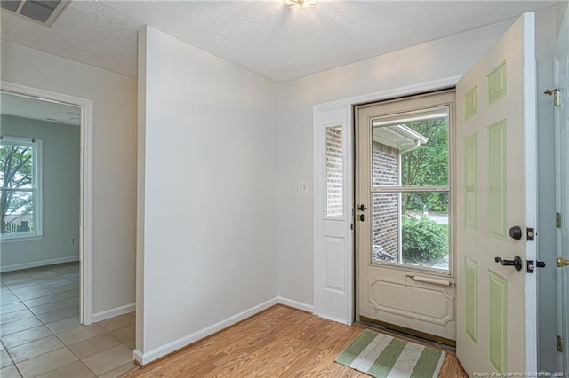 doorway with visible vents, a textured ceiling, baseboards, and light wood-type flooring
