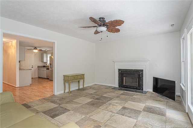 unfurnished living room featuring a ceiling fan, a textured ceiling, a fireplace with flush hearth, and visible vents