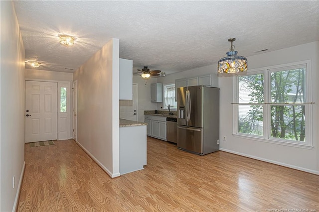 kitchen featuring a textured ceiling, a sink, baseboards, light wood-style floors, and stainless steel appliances