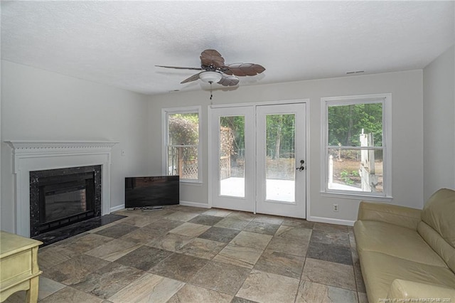 unfurnished living room with a fireplace with flush hearth, baseboards, ceiling fan, and stone finish floor