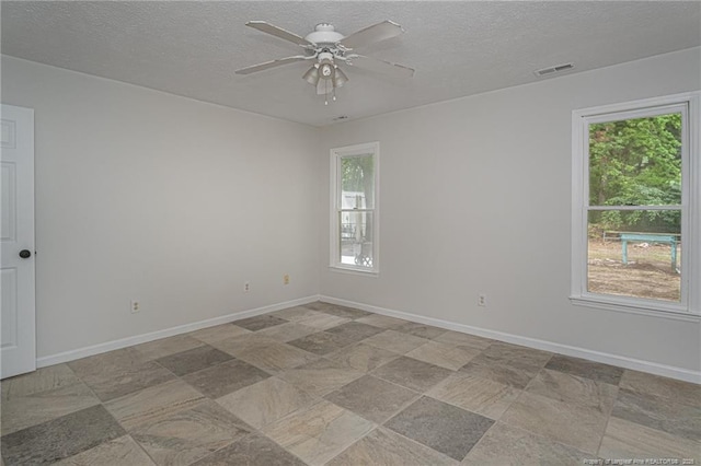 spare room featuring a textured ceiling, ceiling fan, visible vents, and baseboards