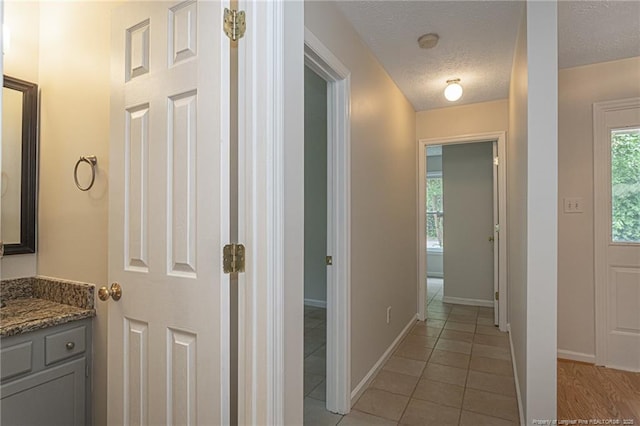 hall with light tile patterned floors, baseboards, and a textured ceiling