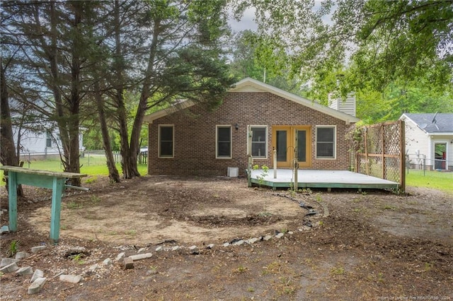 rear view of house with brick siding, a wooden deck, a chimney, and fence