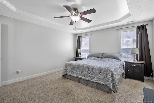 bedroom with light colored carpet, baseboards, a tray ceiling, and multiple windows