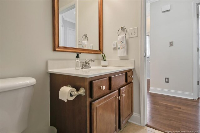 half bath featuring vanity, baseboards, wood finished floors, and toilet