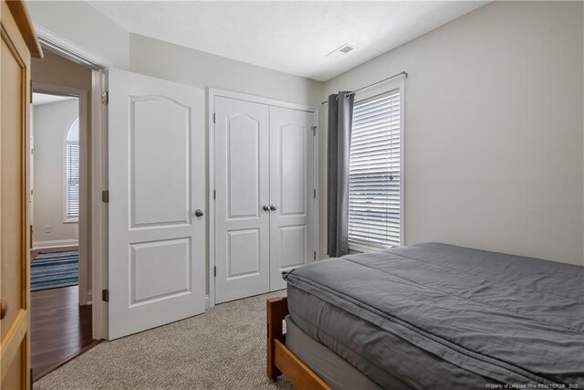 bedroom with a closet, visible vents, and light carpet
