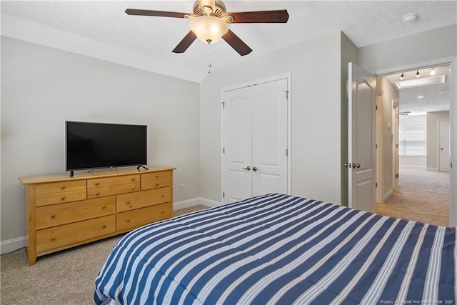 bedroom featuring light colored carpet, rail lighting, baseboards, and a closet