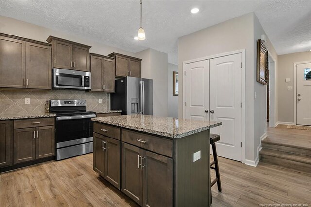 4631 Cedar Pass Dr, Hope Mills, NC 28348 - kitchen with decorative backsplash, dark brown cabinetry, a kitchen breakfast bar, light wood-type flooring, and appliances with stainless steel finishes