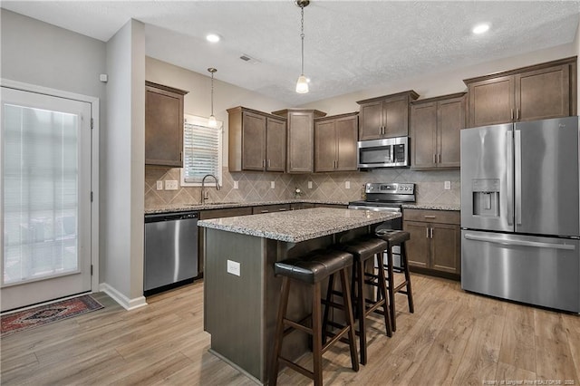 4631 Cedar Pass Dr, Hope Mills, NC 28348 - kitchen with dark brown cabinetry, a kitchen island, appliances with stainless steel finishes, light stone counters, and light wood-style flooring