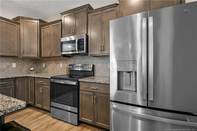 4631 Cedar Pass Dr, Hope Mills, NC 28348 - kitchen with light stone countertops, appliances with stainless steel finishes, dark brown cabinetry, light wood finished floors, and decorative backsplash