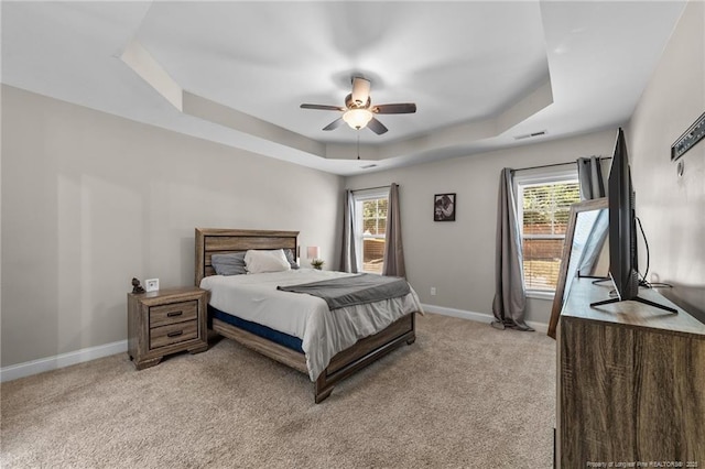 bedroom with baseboards, multiple windows, a tray ceiling, and light carpet
