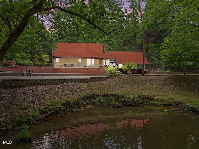 rear view of property featuring a water view, metal roof, and a chimney