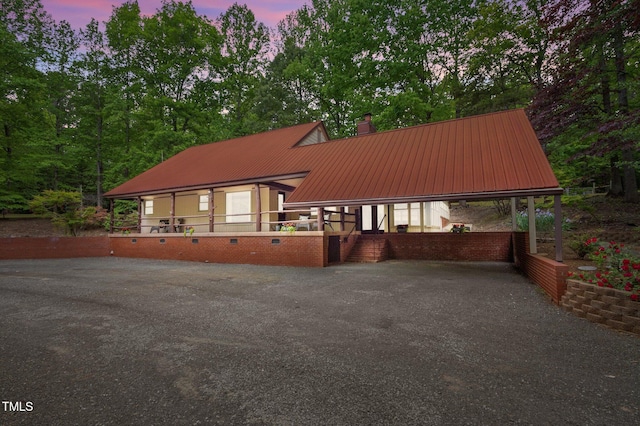 rear view of property with a carport, a chimney, driveway, and metal roof
