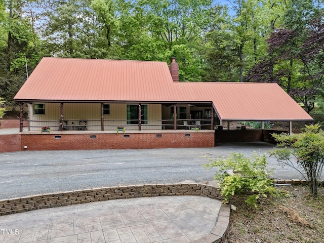exterior space featuring covered porch, a chimney, driveway, and metal roof
