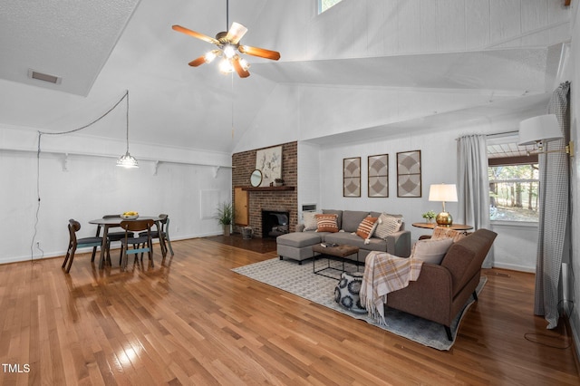 living area with visible vents, wood finished floors, a fireplace, baseboards, and ceiling fan