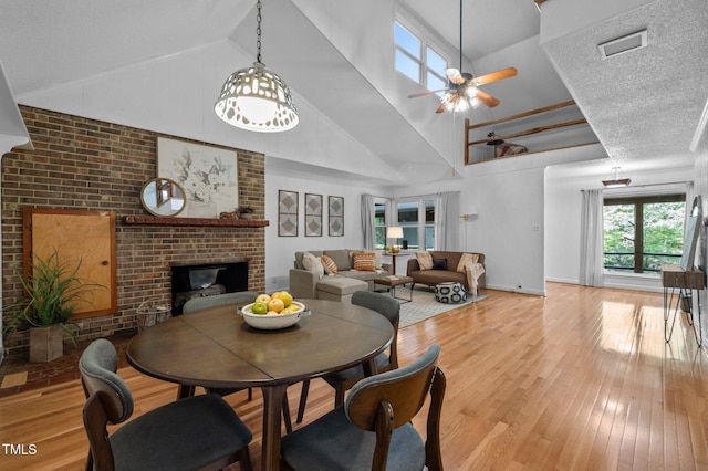 dining space with a ceiling fan, visible vents, a fireplace, high vaulted ceiling, and light wood finished floors
