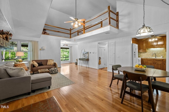 living area with ceiling fan, visible vents, a high ceiling, and light wood-style flooring