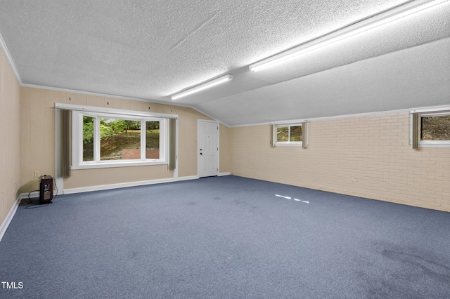 interior space with baseboards, a textured ceiling, lofted ceiling, and brick wall
