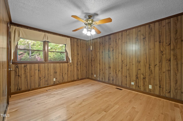 empty room with a ceiling fan, a textured ceiling, visible vents, and light wood finished floors