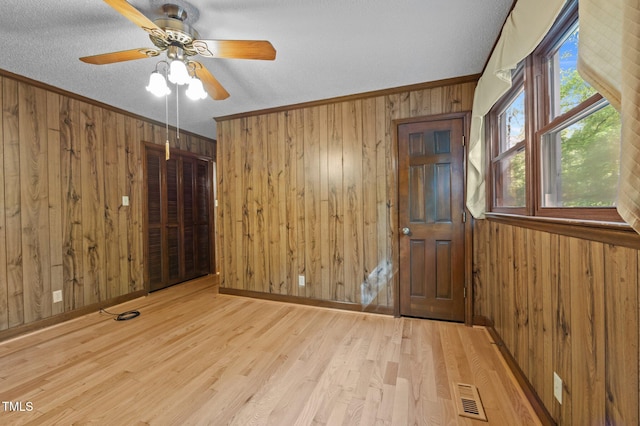 unfurnished room with ceiling fan, wood walls, wood finished floors, and visible vents
