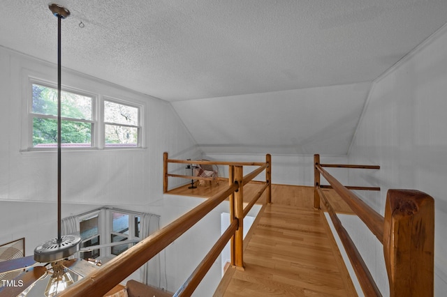hall with a textured ceiling, light wood finished floors, and an upstairs landing