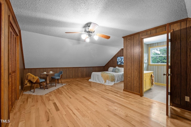 bedroom featuring a textured ceiling, wood walls, baseboards, and light wood-style floors