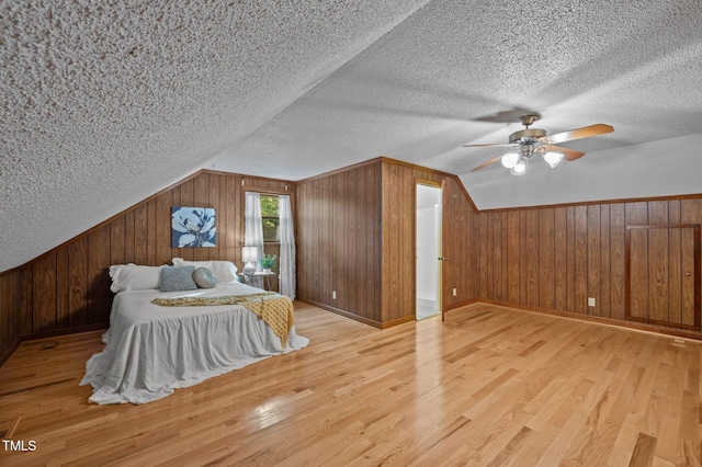 bedroom with wooden walls, vaulted ceiling, a textured ceiling, and wood finished floors