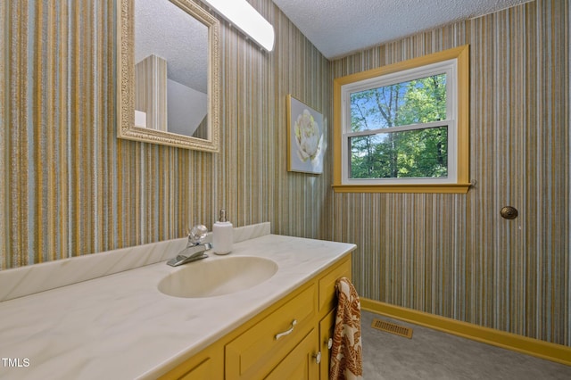 bathroom with vanity, visible vents, baseboards, wallpapered walls, and a textured ceiling